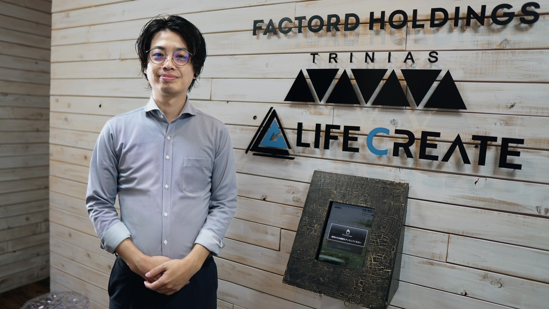 株式会社ライフクリエイトのロゴが入った壁の前に立つ、カスタマーサクセス事業部 事業部長の大湊 竜太様